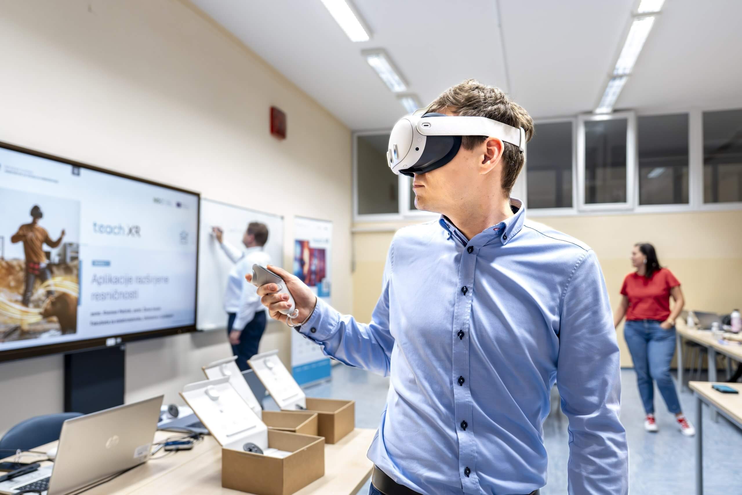 Predavatelj v modri srajci s krmilnikom v desni roki testira delovanje očal za navidezno resničnost.