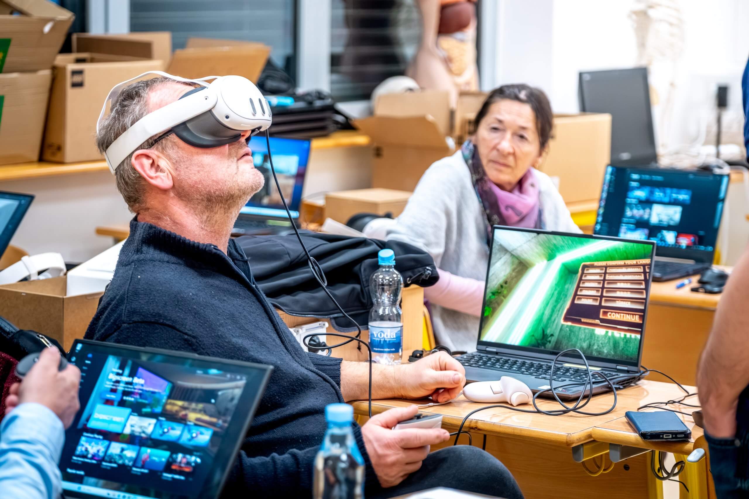 Tri udeleženke, na levi, z mobilnimi telefoni v rokah in 360° kamerami, s pomočjo mentorja na desni testirajo aplikacijo Insta360 za zajem 360° posnetkov.